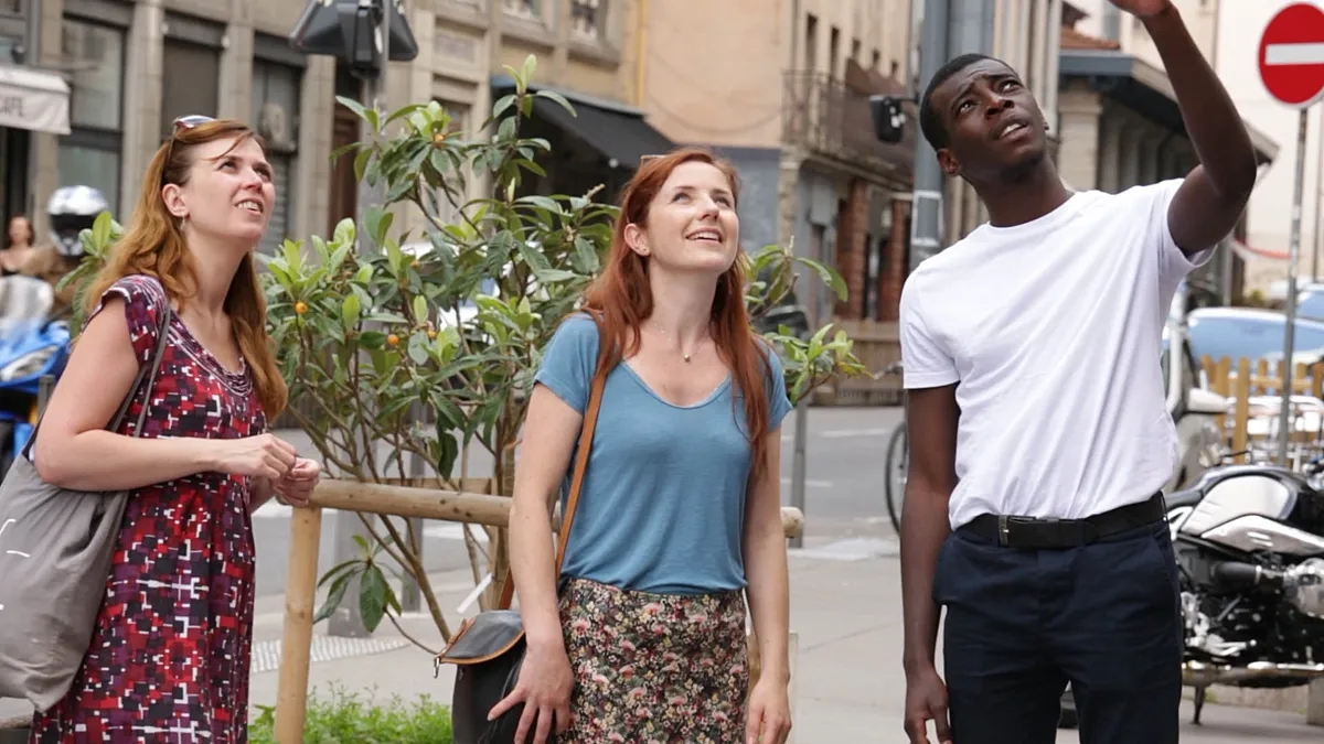 Three French actors look off screen at a mural.